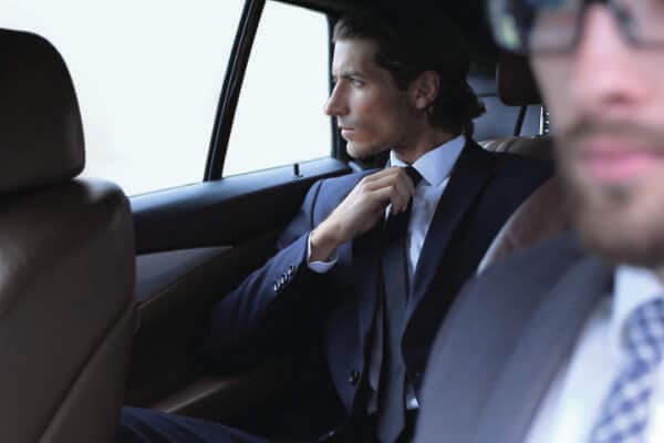 Photo of businessman sitting in the back of a luxury private car while a professional driver is taking him to the airport