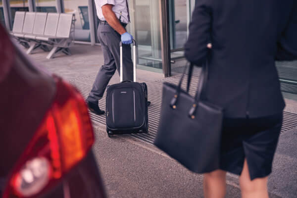 Photo of a businesswoman getting walking away from the private car service that dropped her off at the airport. A porter is taking her luggage inside in the background.