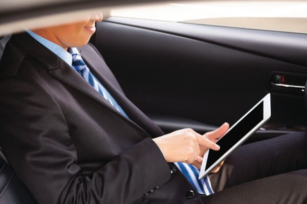 Photo of a businessman working on his tablet in the back of a corporate car.