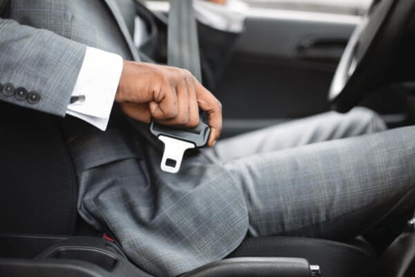 Photo of the side of a man in a grey suit. He is buckling up in the back seat of a corporate car service.