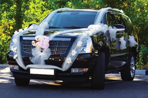 Photo of an SUV decorated with sheer cloth streamers and a teddy bear couple on the grill. It's decorated for a wedding.