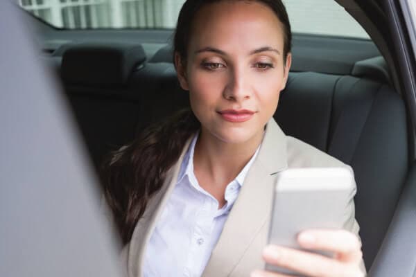 Photo of corporate woman checking her phone while she is being driven by a professional driver.