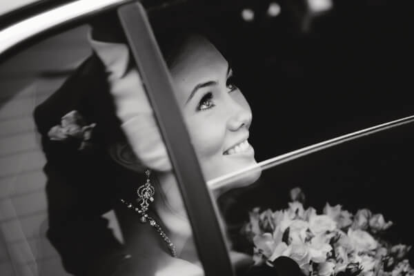 Greyscale photo of bride looking up from the window of a luxury SUV